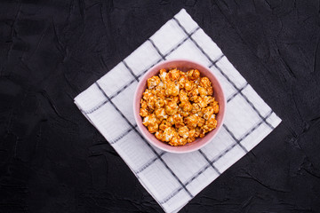 Bowl with golden popcorn on white checkered background. Flat lay conception of rest by watching film. From top view.