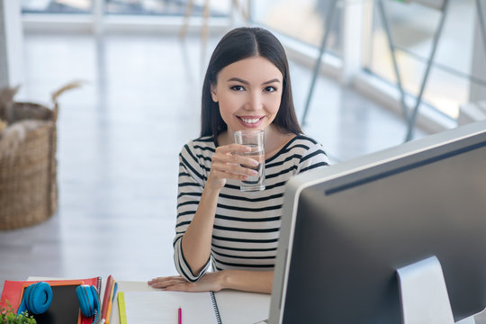 Pretty dark-haired smiling woman holding a glass of water