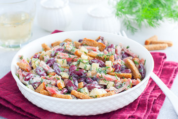 Salad with red beans, smoked sausage, cheese and crackers in a white bowl, horizontal