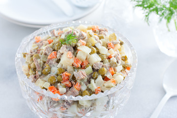 Classic festive salad Olivier in a crystal salad bowl on a white table, horizontal