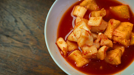 Korean Radish Kimchi in white bowl on wood table for food content.