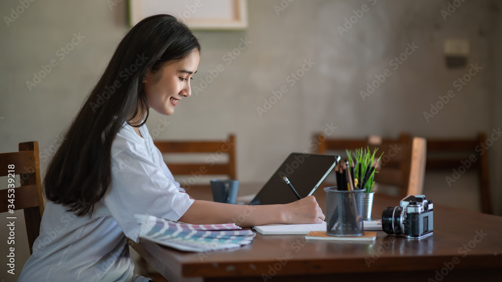 Poster young asian female designer using graphics tablet while working with computer at home.