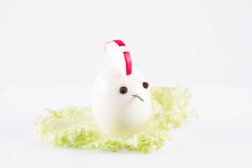 Egg shaped like an animal (with elements made of rosemary, radish, pepper) on a lettuce leaf on a white background