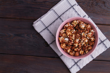 Close up popcorn covered chocolate in pink bowl on dark wooden background. Homemade chocolate popcorn. Concept of watching tv at home.