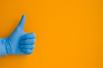 Hand in blue medical glove folded into a fist thumb up excellent sign on an orange background with place for text