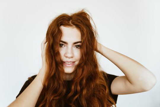 Young Beautiful Girl With Red Hair Very Dense And Curly Waves Shag Their Hand On A Gray Background