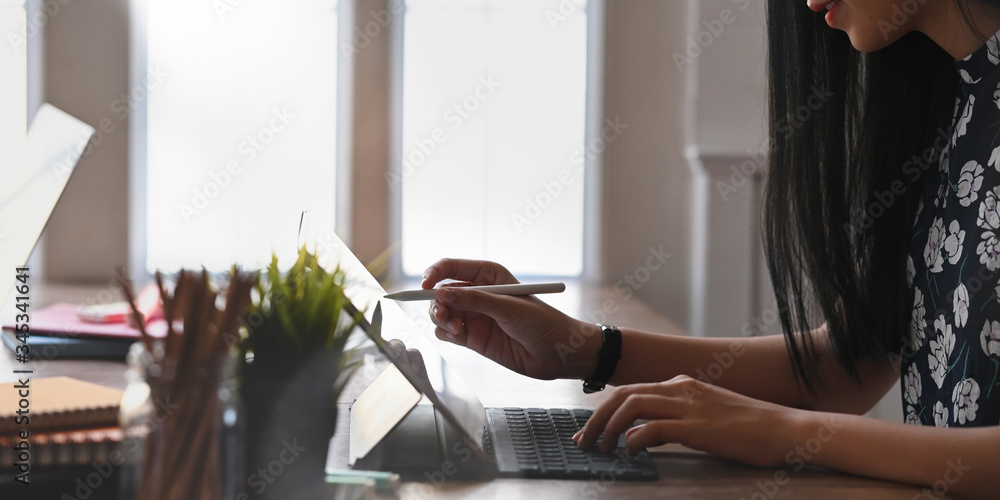 Poster cropped image of beautiful woman sketching on computer tablet by using a stylus pen and sitting at t