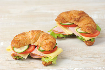 Two croissants with filling.  Croissant filling consists of slices of ham, cheese, tomato, cucumber and lettuce.  Light wooden background.  Close-up.