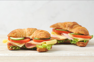 Two croissants with filling.  Croissant filling consists of slices of ham, cheese, tomato, cucumber and lettuce.  Light wooden background.  Close-up.