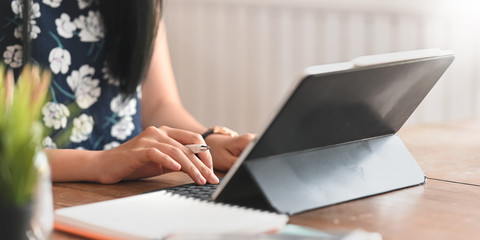 Cropped image of stylish woman holding a stylus pen and typing on computer tablet keyboard case...