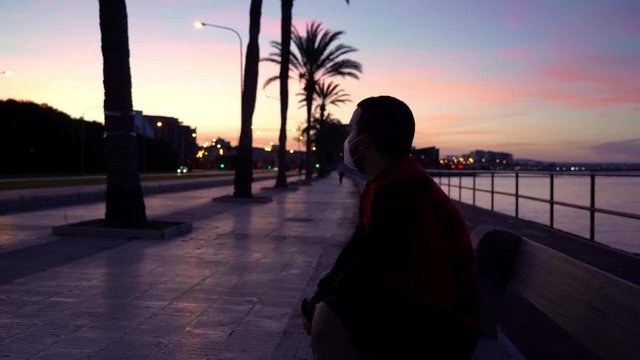 New normal: a roller skater rests on a bench between the sea, some palm trees and the city during sunrise while some birds fly on his back during the permission to practicing sport during covid crisis