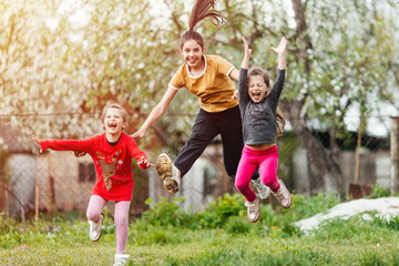 Fototapeta premium happy little girls sisters and twins jumping and playing in the garden with grass