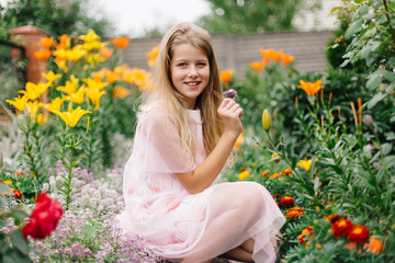 beautiful blue-eyed girl with long blond hair. little girl in a pink flamingo dress. girl in the flower garden. summer bright, emotional photo. large, thick, bright flower garden near the house. 