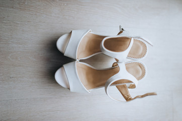 Fototapeta na wymiar Wedding white women's shoes for the bride, sandals are on the floor. Photography, concept, top view. Morning and preparation for the holiday.