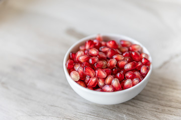 Pomegranate seeds in a small white bowl on a beige background