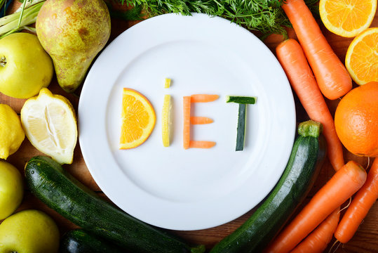 palabra dieta escrita con frutas i verduras sobre un plato blanco y rodeado de alimentos saludables