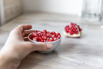 Hand holds a small white bowl with pomegranate seeds on a beige background