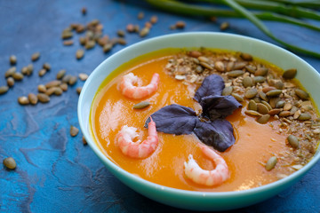 close up pumpkin soup with green onions and prawns on a blue background. Top View