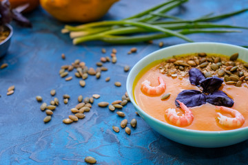 pumpkin soup with green onions and prawns on a blue background. Top View