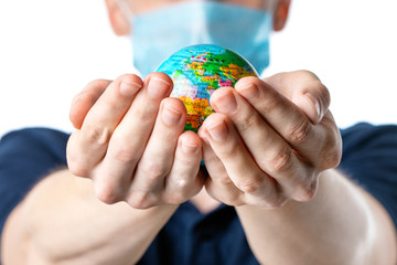 Close-up of a man's hands holding a small globe, with images Europe, a man in a medical mask out of focus, dressed in a blue t-shirt on a white isolated background. Coronavirus, Covid-19