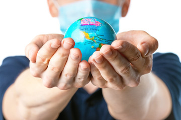 Close-up of a man's hands holding a small globe, with images USA, Canada, Bahamas, Cuba a man in a medical mask out of focus, dressed in a blue t-shirt,  on a white isolated background. Coronavirus