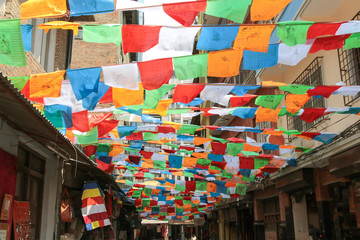 Colourful tibetan buddhist prayer flags waves above Shree Gha Bihar Road with souvenir shops in...