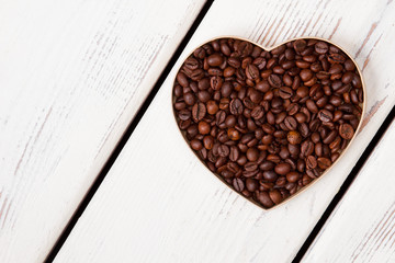 Heart shaped coffee beans on white wooden board. Top view close up.
