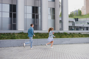 Romantic and happy caucasian couple in casual clothes walking together through the streets. Love, relationships, romance, happiness concept. Man and woman with disposable cups of coffee in the city.