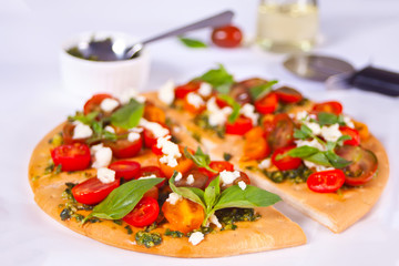 Homemade pizza with cherry tomatoes, fresh green basil and feta cheese. Homemade food. Concept for a tasty and hearty meal. Wooden background. Close up.