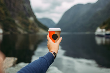 female hand with a clock holds coffee on the background of the river, mountains