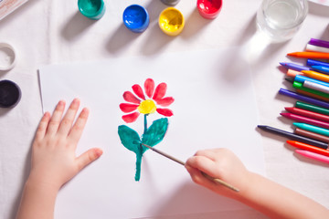 A child draws flower with colored paints on the paper.