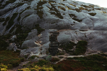 a girl in a yellow raincoat goes down the stone steps in the mountain of norway
