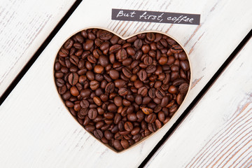 Close up roasted coffee beans forming heart form. But first coffee. Top view flat lay.