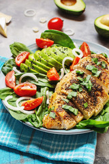 Grilled chicken breast and avocado salad with spinach and cherry tomatoes on concrete background. Healthy food, ketogenic diet