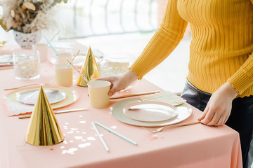 Woman serving party table in pastel colors with pink tablecloth, paper colorful dishes, cups and golden cutlery. Happy birthday for girl. Selective focus