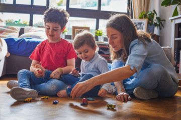 Happy family, mother and children play in the living room with some toy cars.