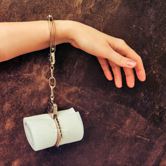 A woman's hand is handcuffed to toilet paper, a background of dark brown stone. Concept of stomach...