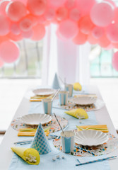 Decorative festive table setting for kids party dinner with textile napkin and tablecloth in sky blue and yellow colors . Pink balloons decoration