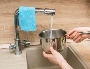 hands pour water into a pan for cooking in the kitchen in the house