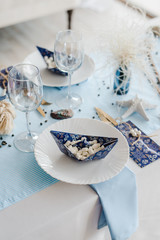 Party table setting in sea style. Elegant white plates, glasses, in blu? colors. Paper boats with marshmallow. Birthday or baby shower boy concept.