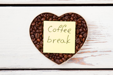 Coffee break and love concept. Brown roasted coffee beans in a heart shape form on white wooden background.