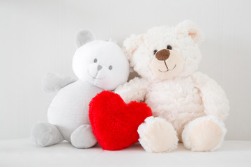 Two smiling white teddy bears sitting on bed. Red fluffy heart. Togetherness and friendship concept. Kids best friends. Front view. Closeup.