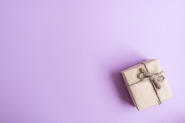 Gift in eco-friendly packaging made of craft, recycled paper on a light, lilac background.