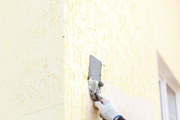 Male builder smear gray wet plaster with a spatula on the facade of the house