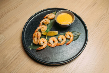 fried shrimp on a green leaf with a slice of orange and yellow sauce on a black plate