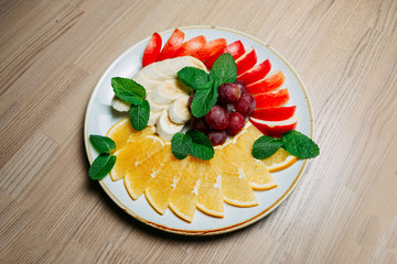 fruit sliced banana apple orange and grape with mint leaves on a white frosted plate