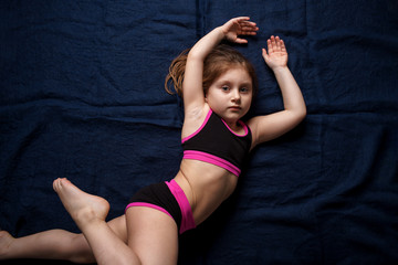 Fototapeta na wymiar A white-skinned girl lies on a blue background in a beautiful pose. Sports girl. Childhood. Sport. Close-up.