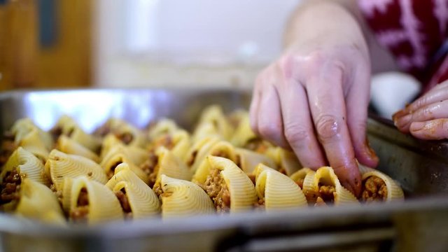 Preparation of homemade lumaconi filled in with tomato sauce and minced meat. Close up of man's hands stuffing homemade Italian pasta recipe