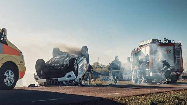 On the Car Crash Traffic Accident Scene: Paramedics and Firefighters Rescue Injured Victims Trapped in the Vehicle. Medics Use Stretchers, Perform First Aid. Firemen Grab Equipment from Fire Engine
