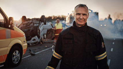 Portrait of the Brave Firefighter Smiling on Camera. In the Background Courageous Heroes Paramedics...